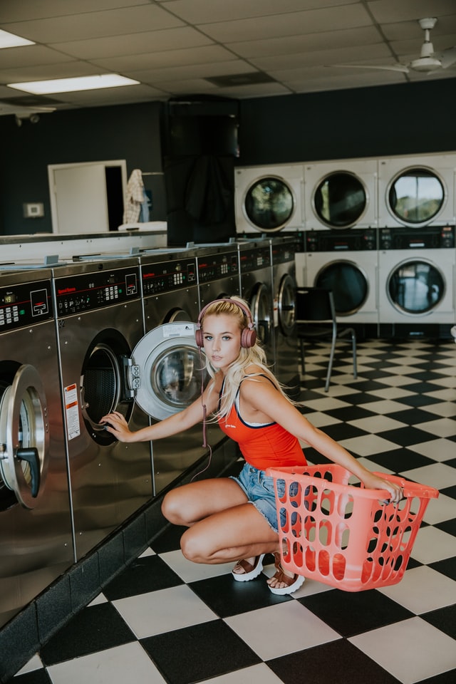 Woman kneeling and holding orange basket in front of front load washing machine inside a laundry shop